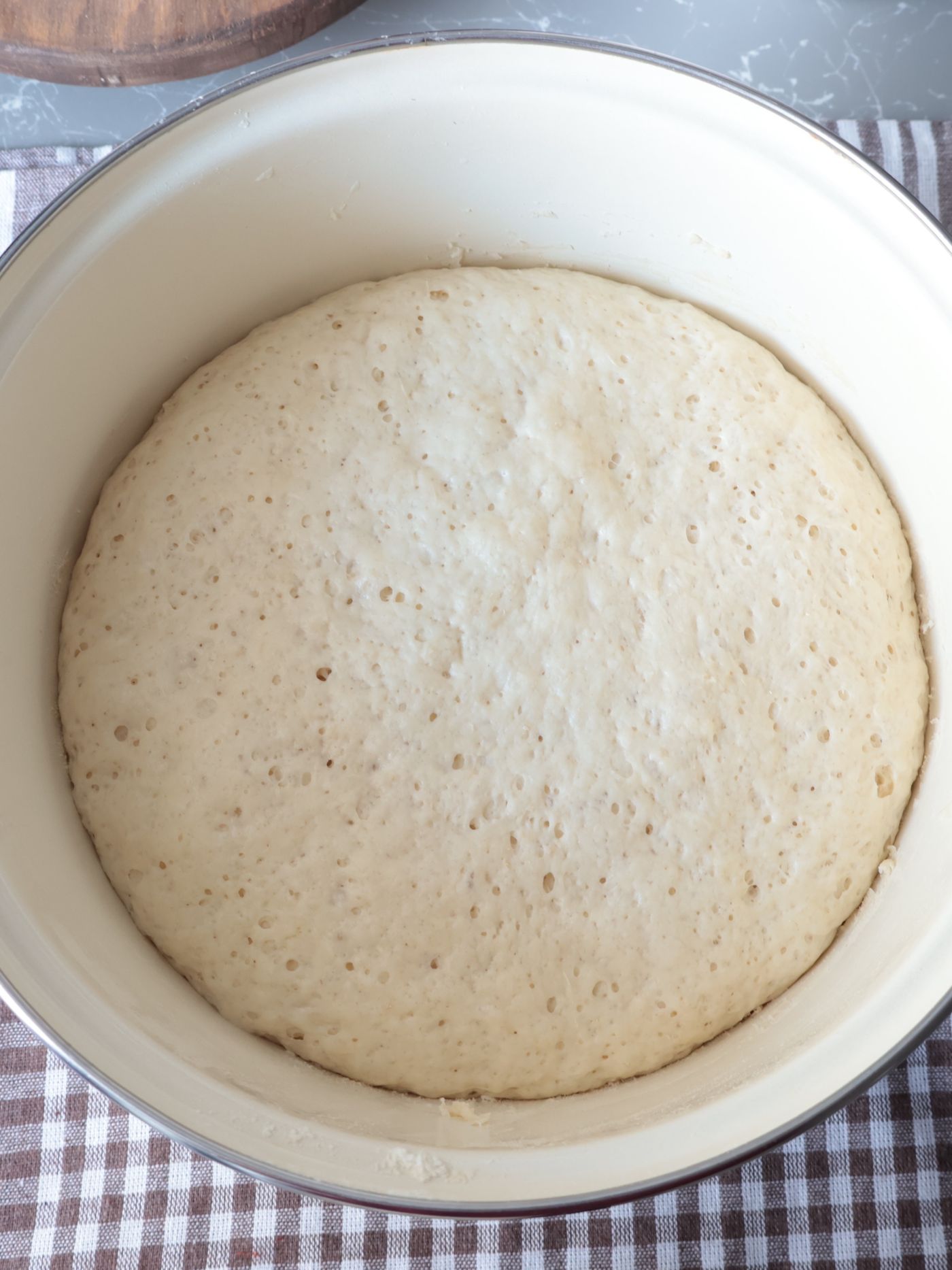 Smooth risen dough filling a white bowl on a checked tablecloth