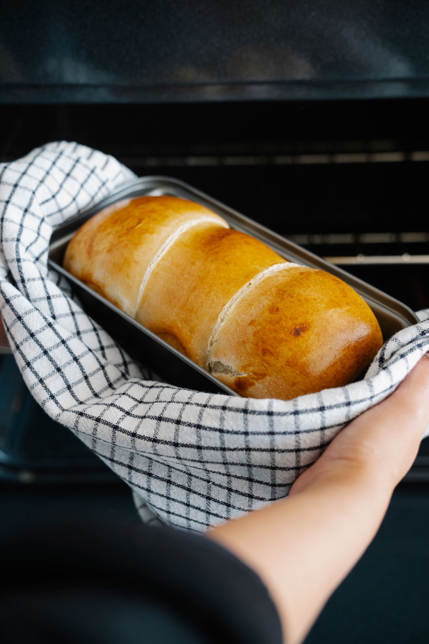 Hands placing a tray of bread dough into a hot oven